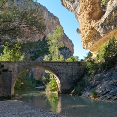 Photographie d'une rivière encaissée calme et au niveau bas passant sous l'arche d'un petit pont de pierre
