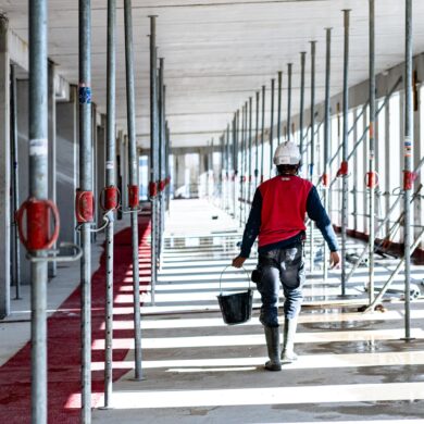 Vue d'un ouvrier de dos avançant en portant un seau à la main dans un alignement d'étais manchon