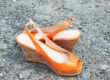 Photographie de rue focus sur une paire de chaussures de femme orange à semelles compensées sur fond de sol gravilloneux