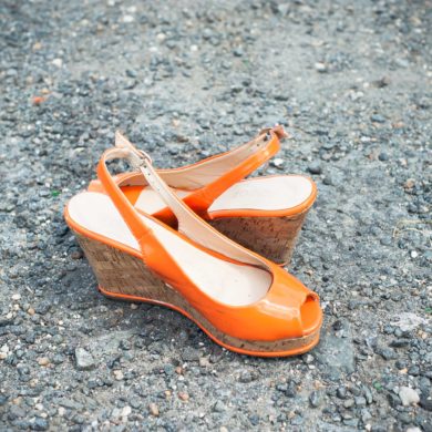 Photographie de rue focus sur une paire de chaussures de femme orange à semelles compensées sur fond de sol gravilloneux
