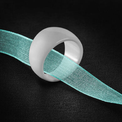 Image carrée d'une bague en céramique blanche traversée par un ruban vert sur fond noir